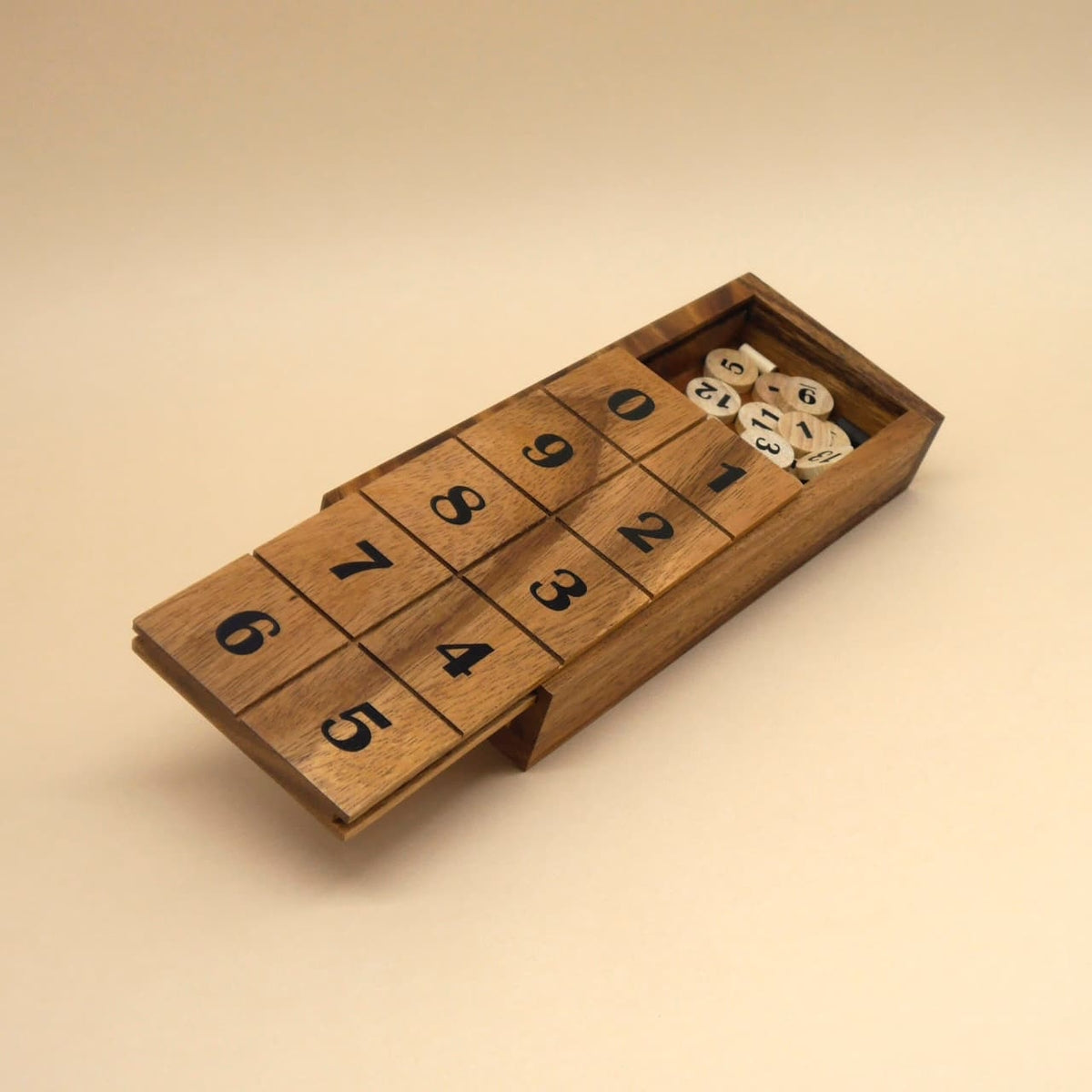 Teilgeöffnetes Holz-Rechenspiel: Schiebedeckel mit Zahlenfeldern 0–9 und darunter sichtbare Zahlenplättchen, fotografiert vor neutralem Beige.