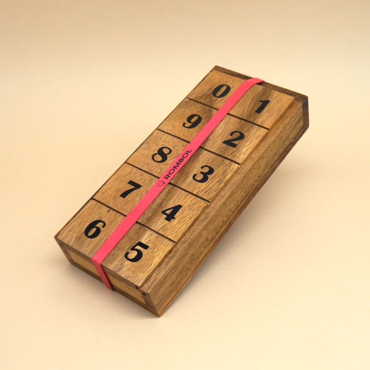 Kompaktes mathematisches Spiel aus Holz, durch ein rotes Gummiband zusammengehalten; Klappen mit den Ziffern 0–9 laufen quer über die Oberseite.