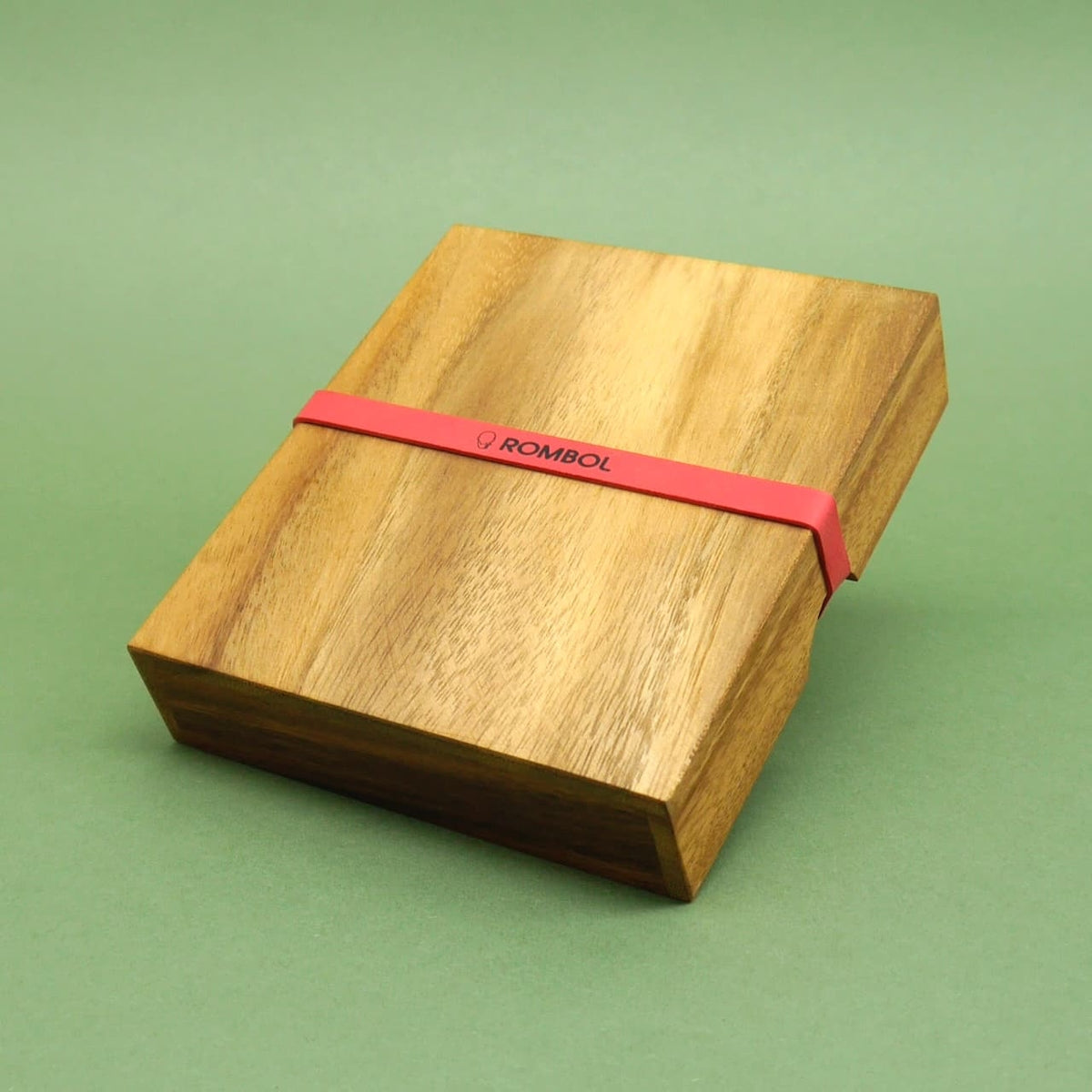 Geschlossenes Schiebepuzzle in schlichter Holzbox, von einem roten ROMBOL‑Gummiband zusammengehalten.