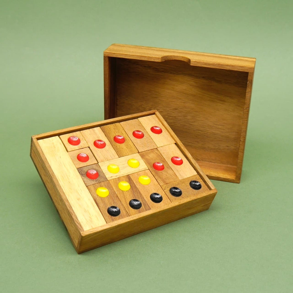 Fertig arrangiertes Schiebespiel aus Holz; farbpunkt‑markierte Steine liegen in einer offenen Box, der Deckel lehnt dahinter.