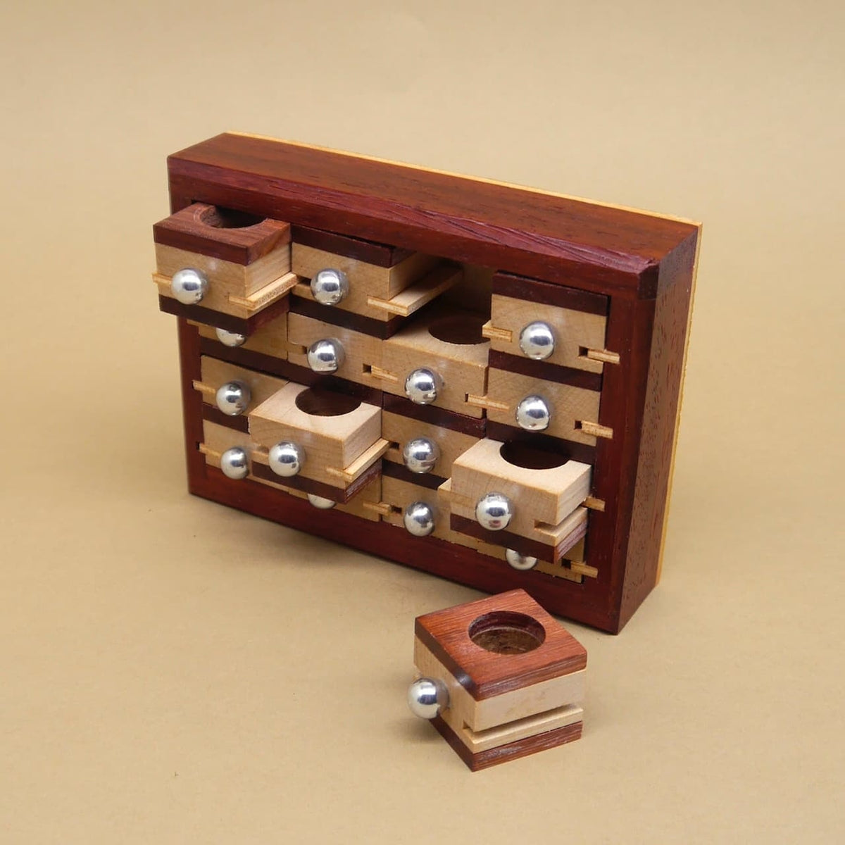 Holzpuzzle in Form eines Apothekerschranks mit herausziehbaren kleinen Würfeln, die jeweils mit einer silbernen Kugel versehen sind, ein Würfel liegt separat davor.