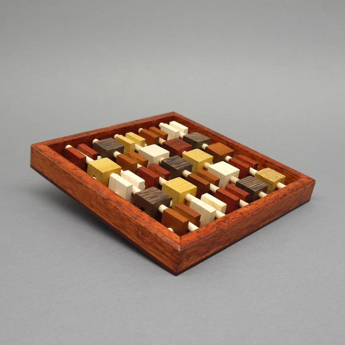 Holzpuzzle ‚Brochettes‘, bestehend aus mehreren länglichen Holzelementen, die zu einem kompakten Würfel oder Block zusammengesteckt werden. Ein anspruchsvolles Denk- und Knobelspiel zur Förderung der räumlichen Vorstellungskraft.