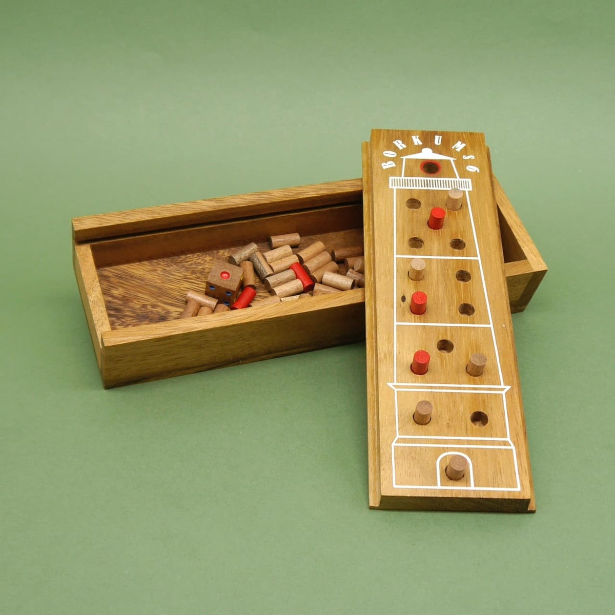 Geöffnetes Holzetui des handlichen Reisespiels „Borkums 6“: Deckel im Leuchtturm-Design lehnt an der Box, daneben liegen Würfel und zahlreiche Holzstifte auf grünem Untergrund.