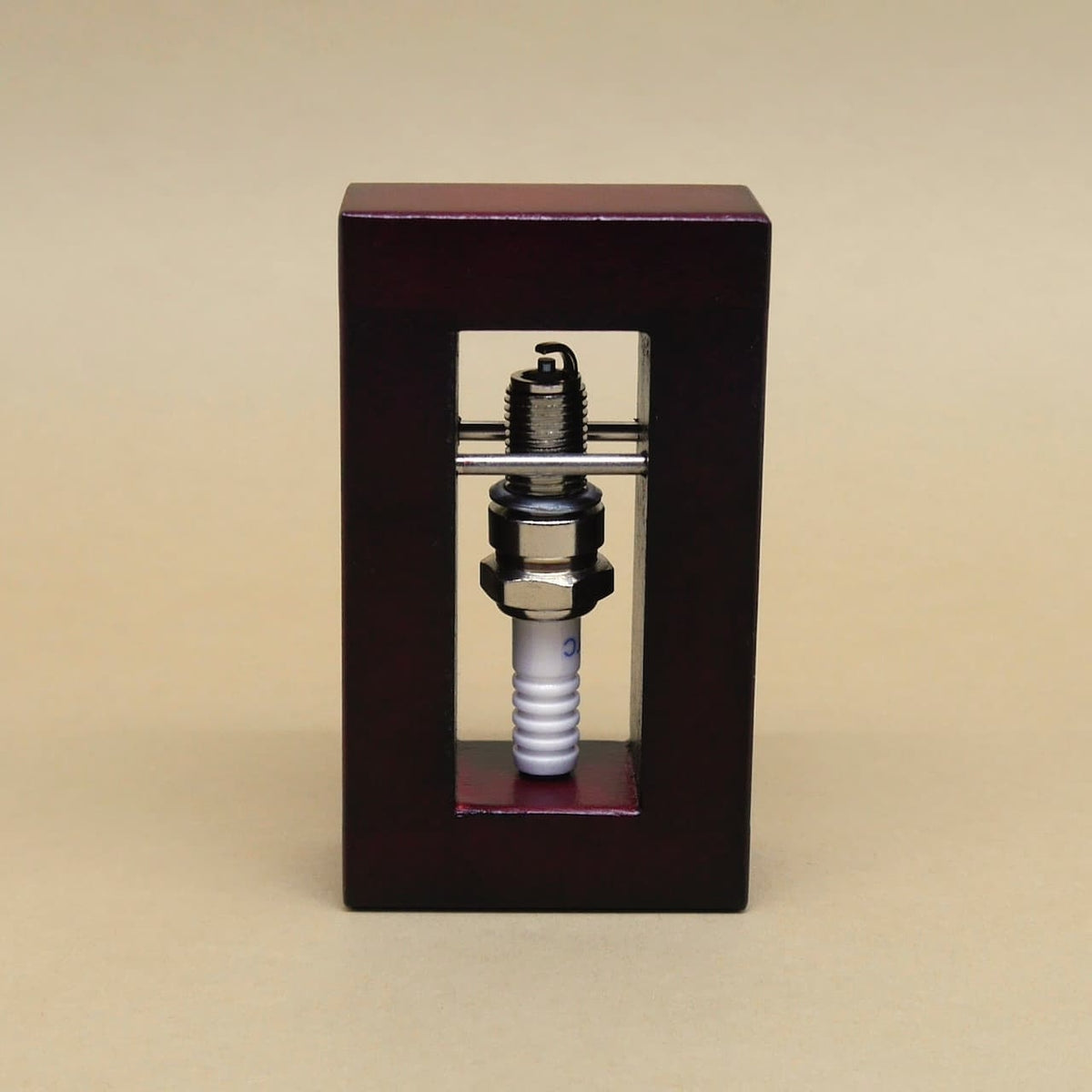 In einem hochkant stehenden Holzrahmen blockieren zwei Metallstangen eine Zündkerze und machen das Holz‑Logikpuzzle zu einem echten Geduldsspiel.