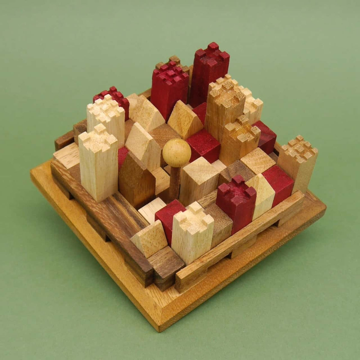 Holzbausteine in Rot- und Naturtönen bilden ein kompaktes 3D-Puzzle in Burgform, dicht an dicht auf einem quadratischen Holzbrett vor grünem Hintergrund angeordnet.