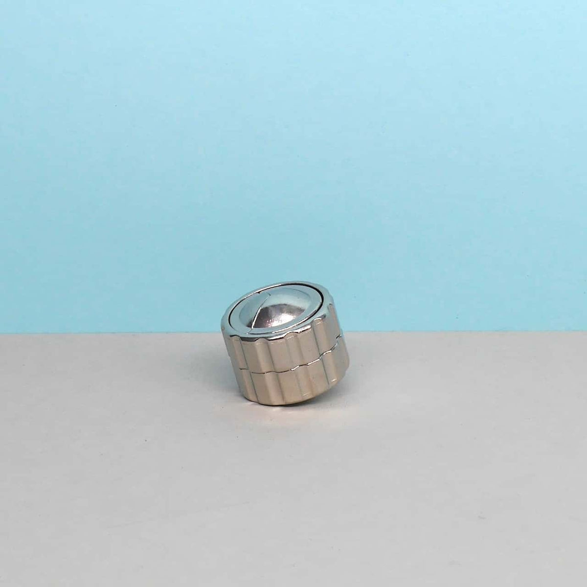 Das silberne Cast Cylinder Geduldspiel liegt leicht geneigt auf einem zweifarbigen Untergrund – eine Herausforderung für Logikliebhaber und Puzzlefreunde.