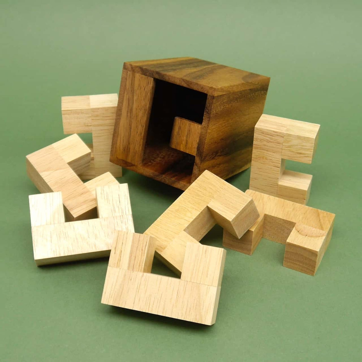 Zerlegte Holzstücke eines 3D-Puzzles liegen vor einer geöffneten Würfelbox auf grünem Hintergrund.