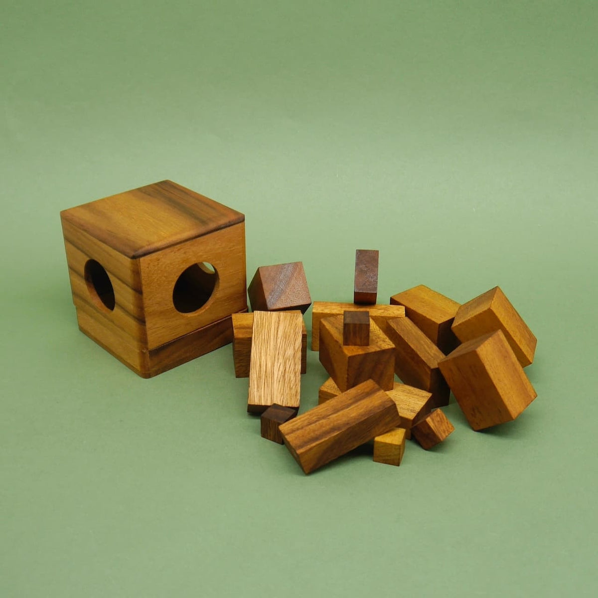Holz-Geduldsspiel: geöffnete Würfelhülle mit verstreuten rechteckigen Klötzchen vor grünem Hintergrund.