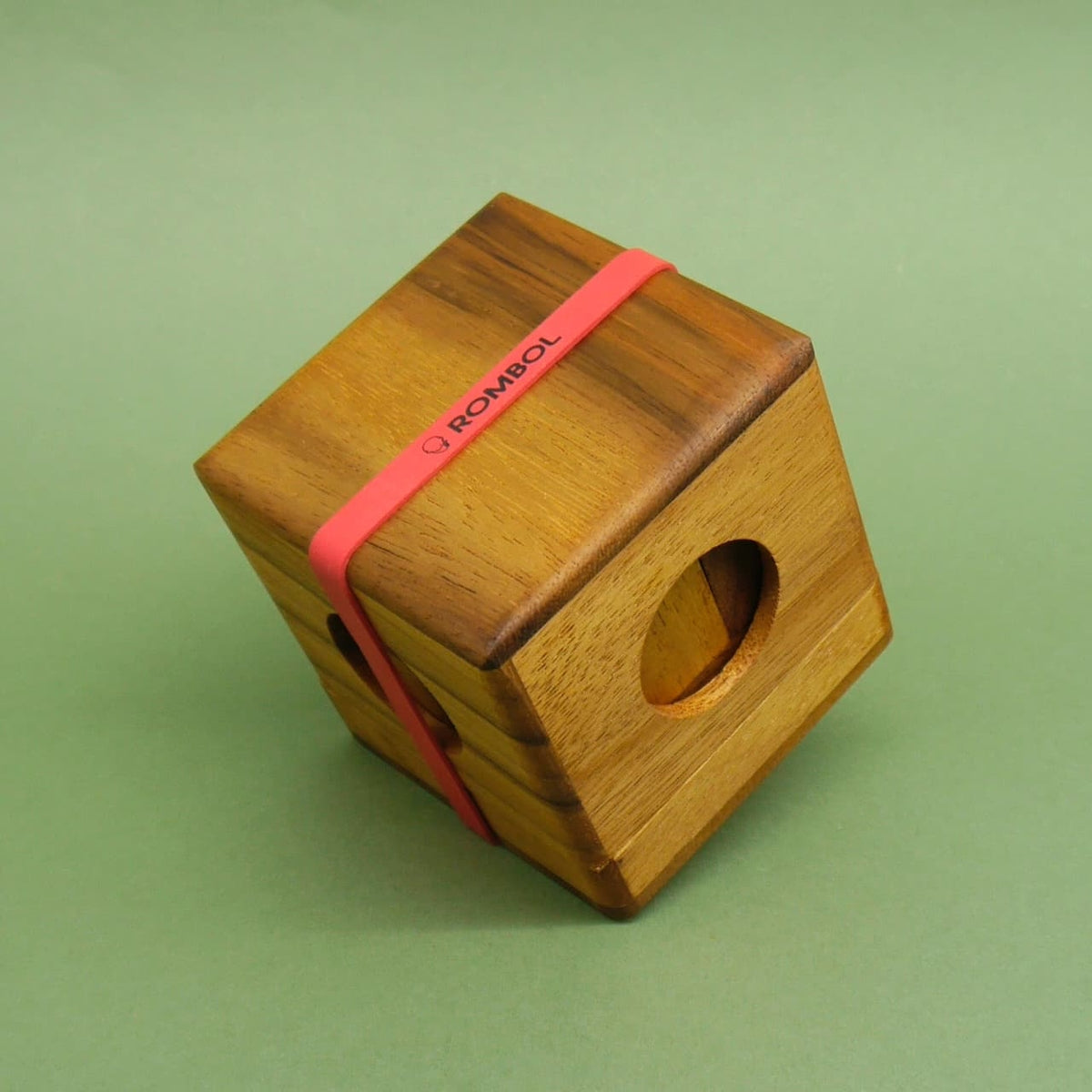 Schräg liegender Knobelspiel-Würfel aus Holz, von einem roten Gummiband mit ROMBOL-Logo zusammengehalten.