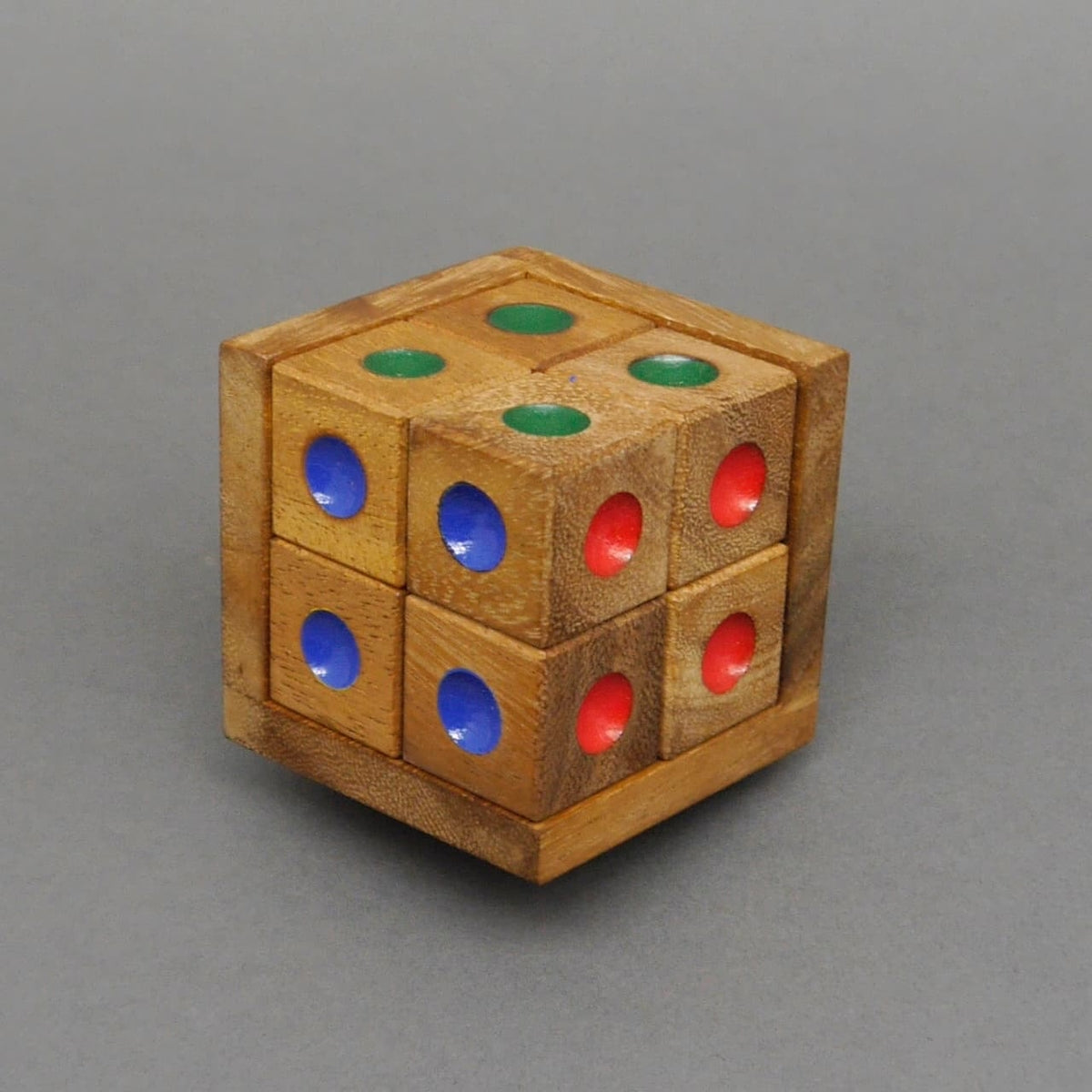 Farbpuzzle-Holzwürfel, komplett zusammengesetzt – sechs kleine Würfel mit grünen, blauen und roten Farbpunkten bilden einen großen Würfel vor grauem Hintergrund.