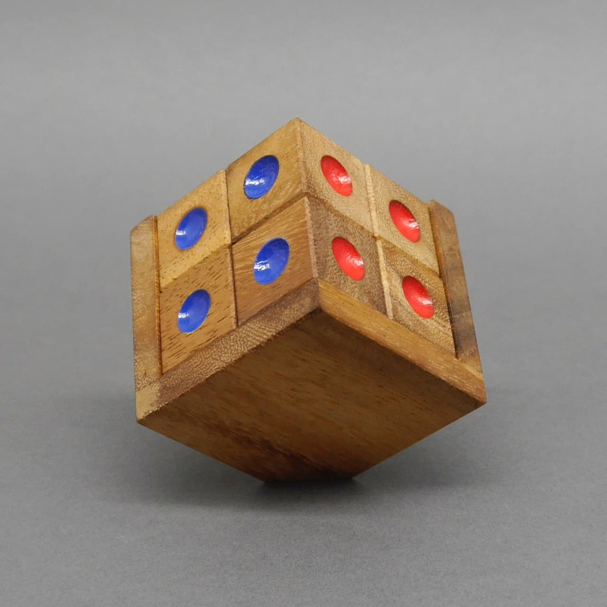 Schräg balancierender Holzwürfel-Knobelpuzzle mit abwechselnden roten und blauen Punktmarkierungen vor neutralem Grau.