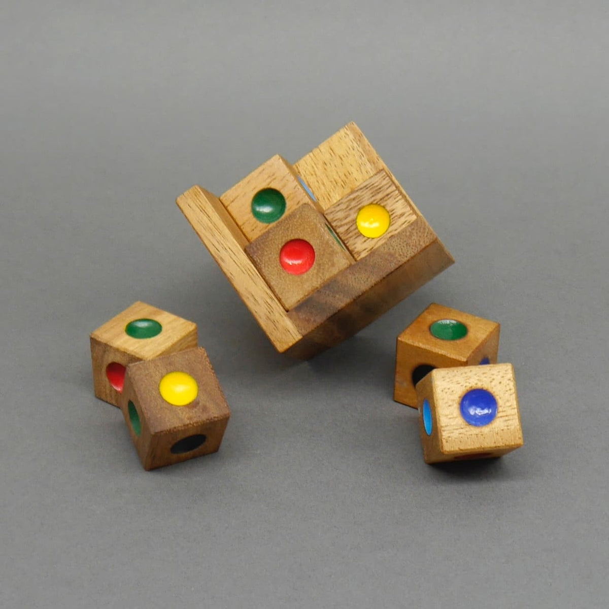 Teilweise gelöster Braingame-Holzwürfel kippt aus seiner Box, umgeben von einzeln liegenden, farbig gepunkteten Holzklötzchen auf grauer Fläche.