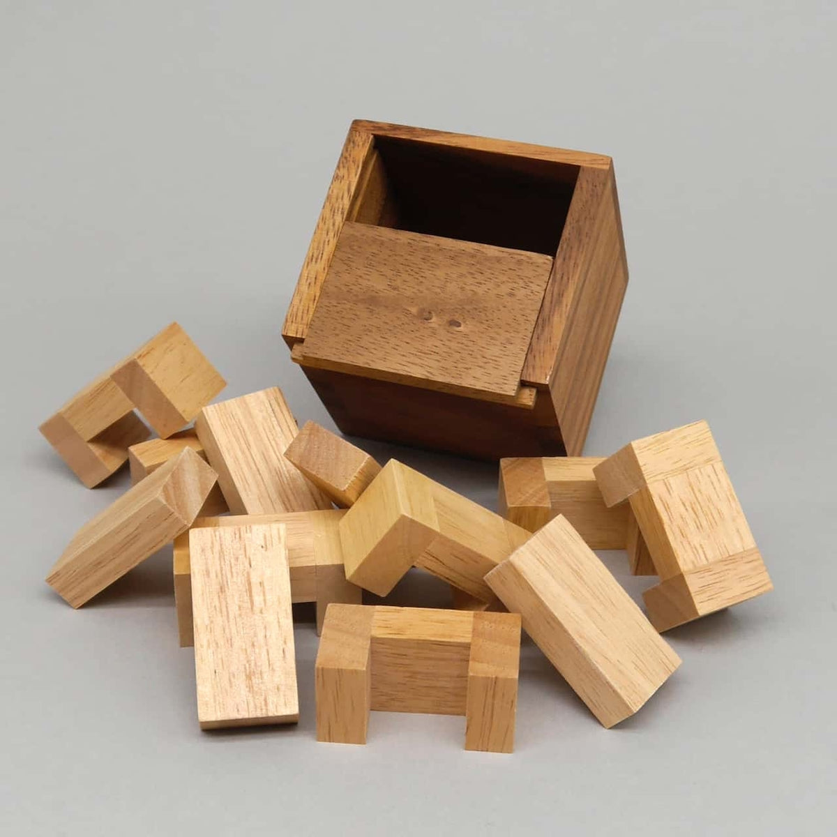 Zerlegtes Holzpuzzle: helle Holzbausteine liegen vor leerer dunkler Box und warten aufs Zusammensetzen.