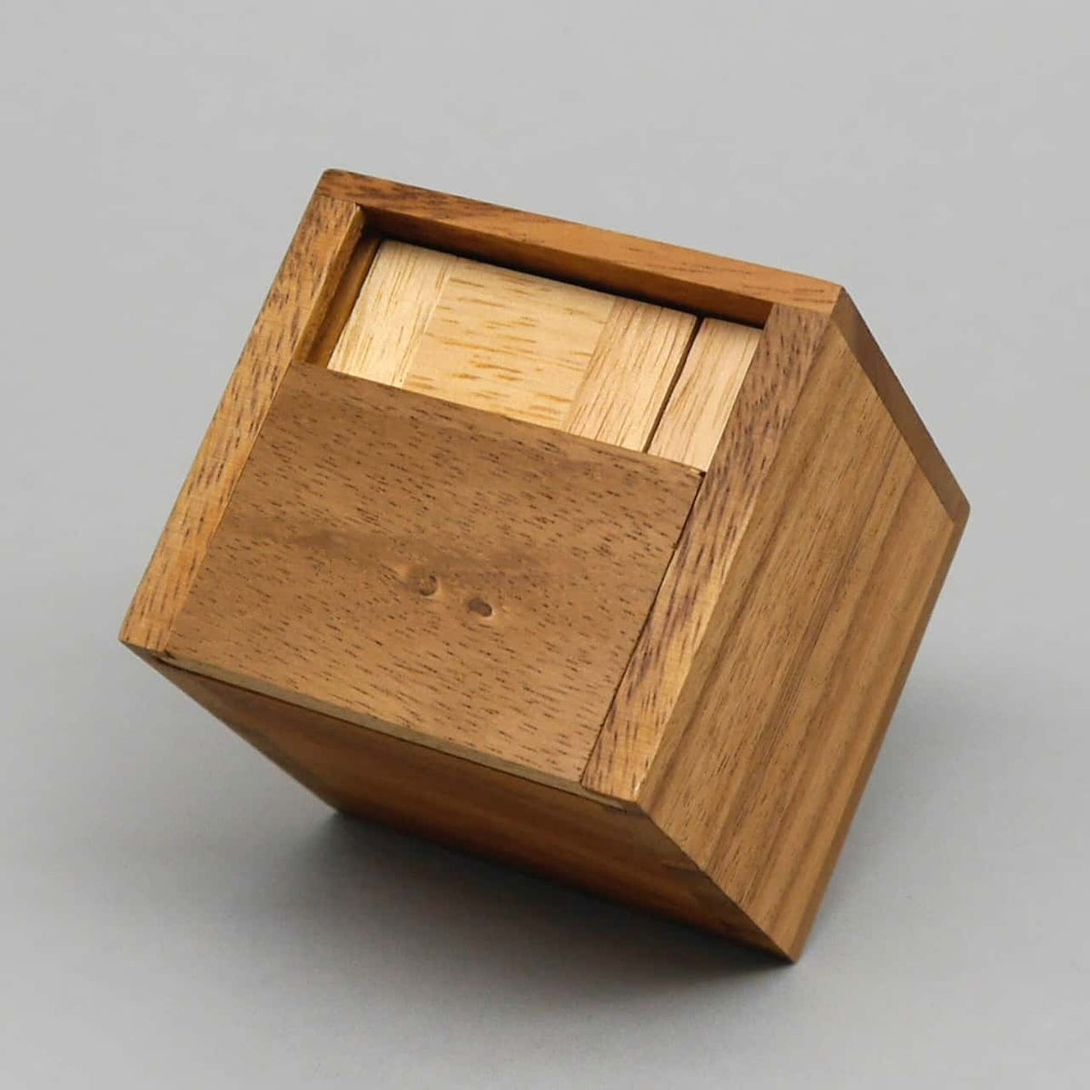 Würfelförmige Knobelbox aus zwei Holzarten, teils geöffnet, mit präziser Schiebemechanik.
