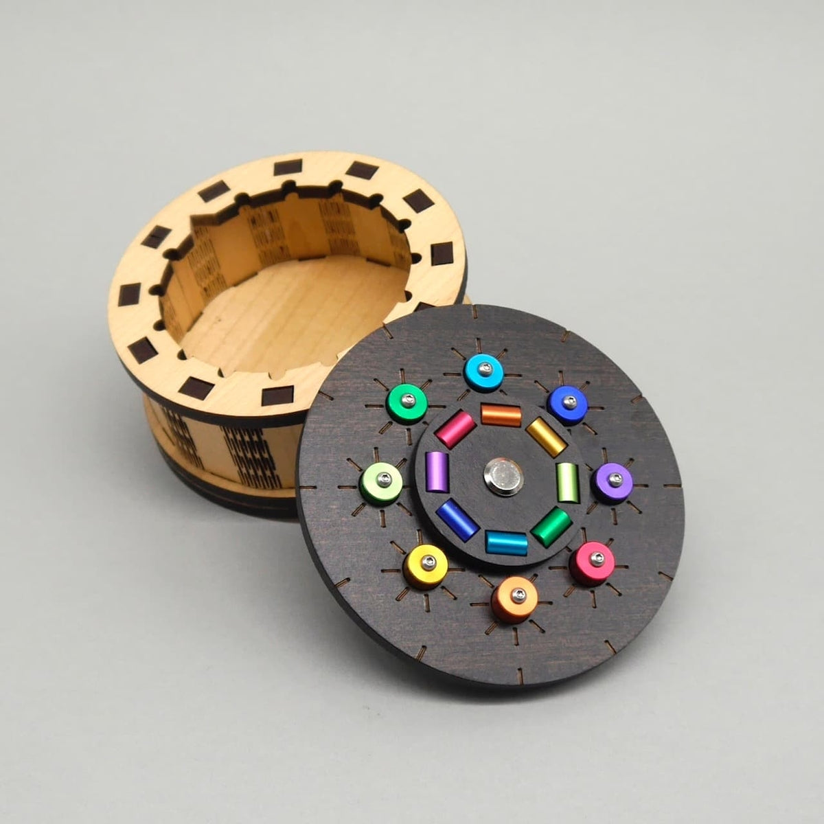 Geöffnete runde Knobelbox aus Holz mit farbigen Elementen auf dem Deckel – die kreative Kombination aus Puzzlebox und Geschenkbox.