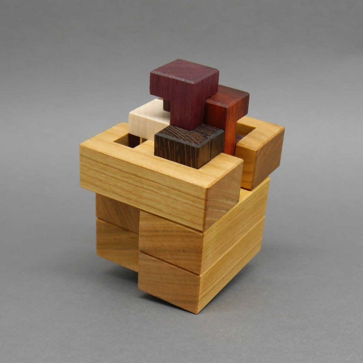 Knobelspiel aus Holz, bei dem einzelne farbige Klötze sichtbar aus einem Würfel herausragen.