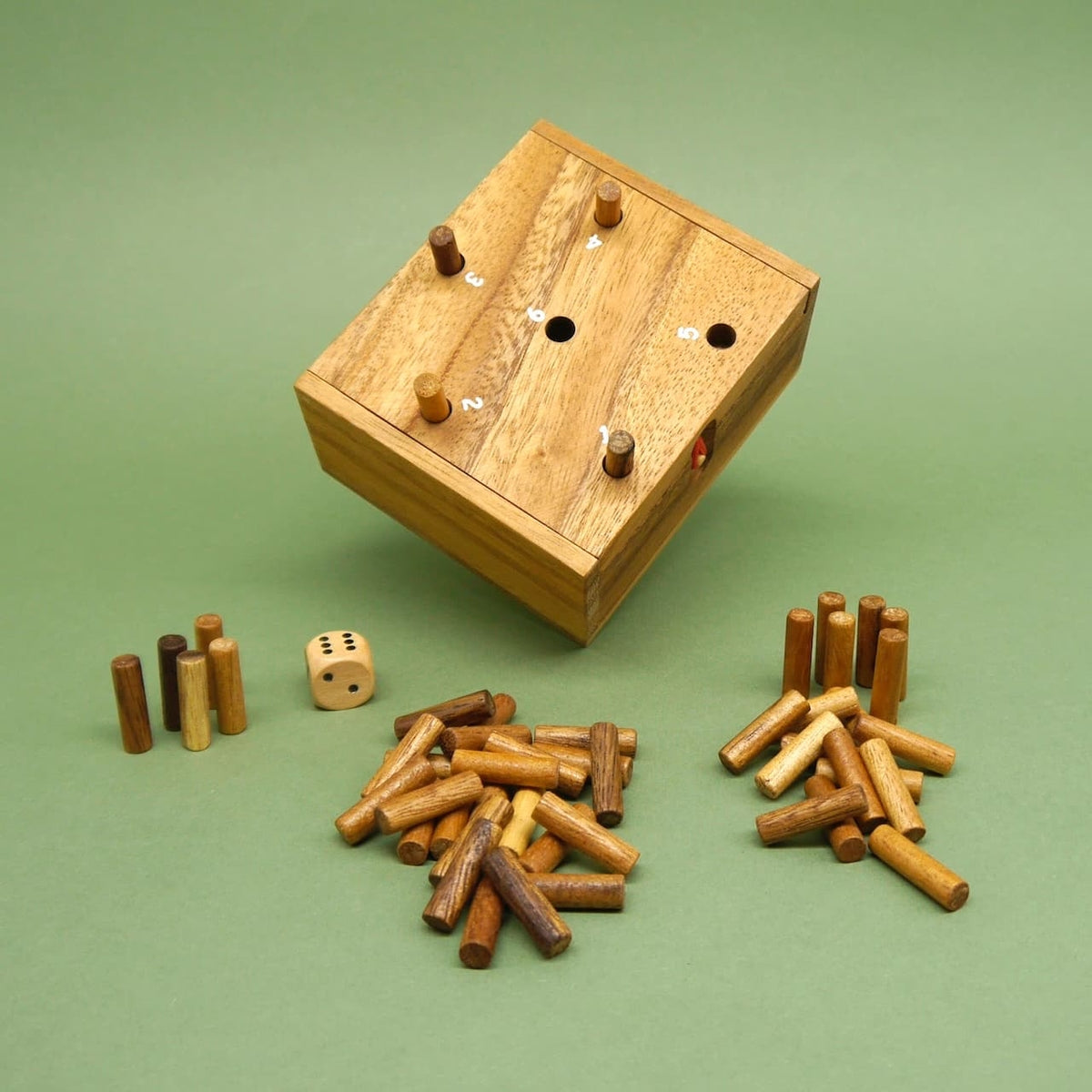 Schräg stehendes Kinderspiel aus Holz: Box mit nummerierten Löchern, ein Würfel sowie sortierte Holzstäbchenstapel davor.