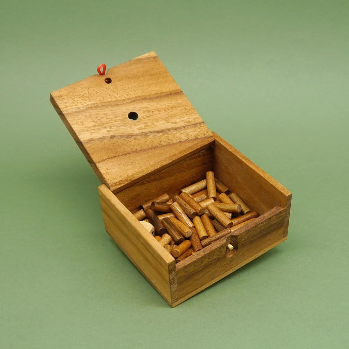 Reisespiel in offener Holzbox: hochgeklappter Deckel zeigt zahlreiche kurze Holzstäbchen und einen Würfel auf grünem Untergrund.