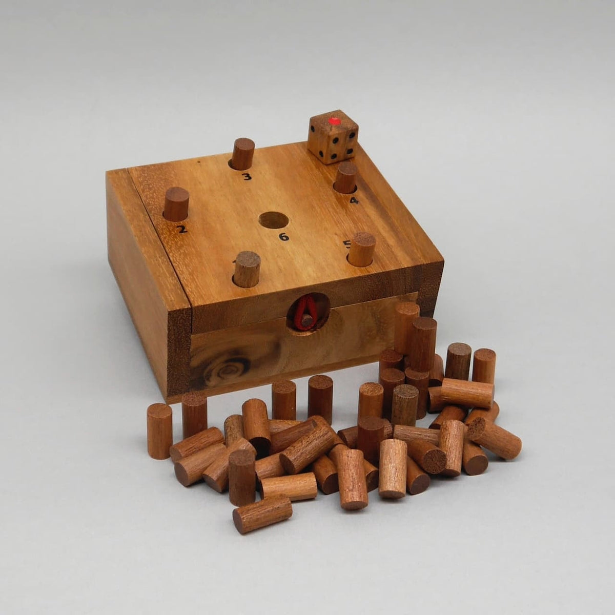 Holzbox des Ferkelspiels mit nummerierten Löchern, eingesetzten Stiften, oben ein Würfel und viele Holzstifte davor.