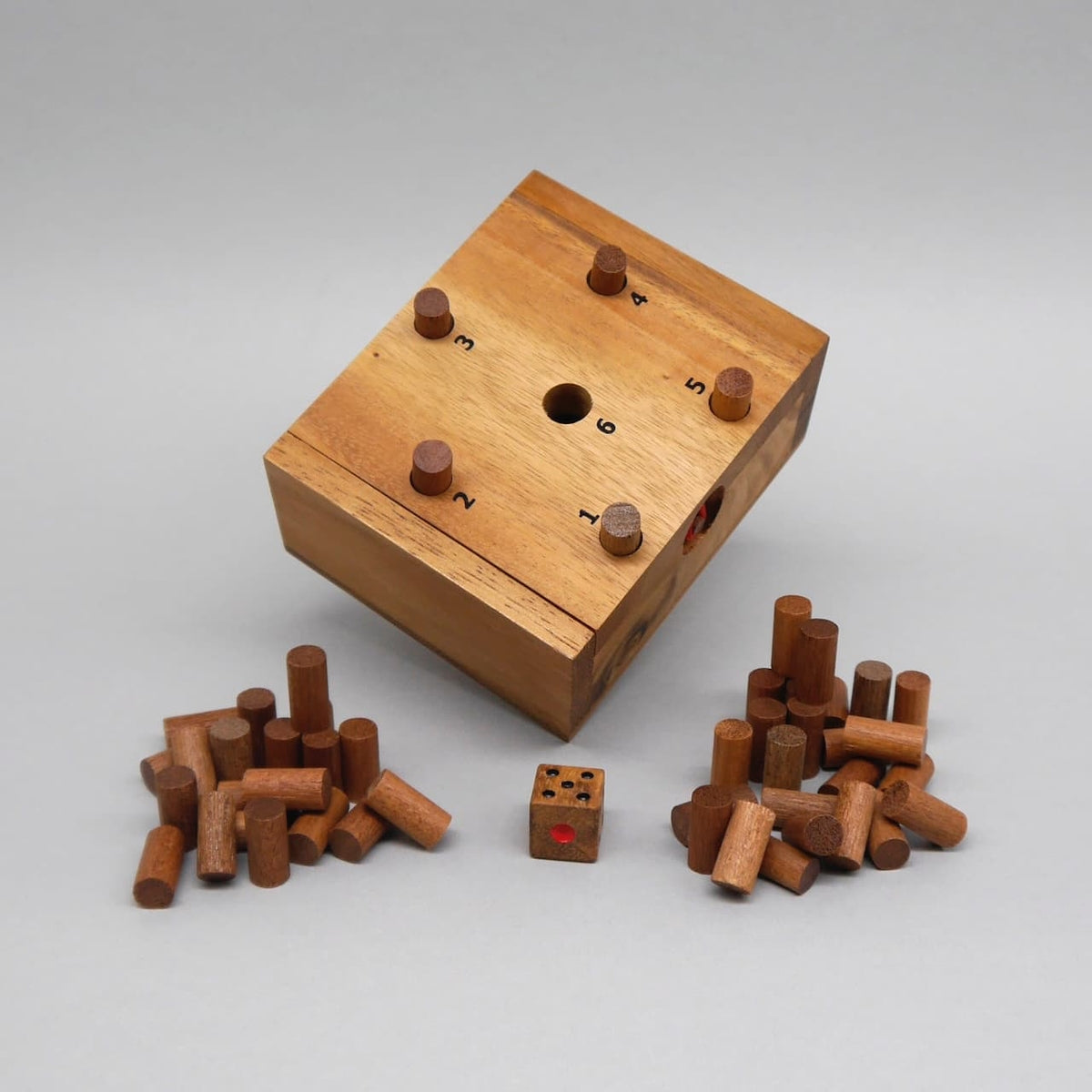 Schräg liegendes Holz-Würfelspiel: nummerierte Löcher mit Stiften, davor Würfel und zwei Haufen Holzstifte.