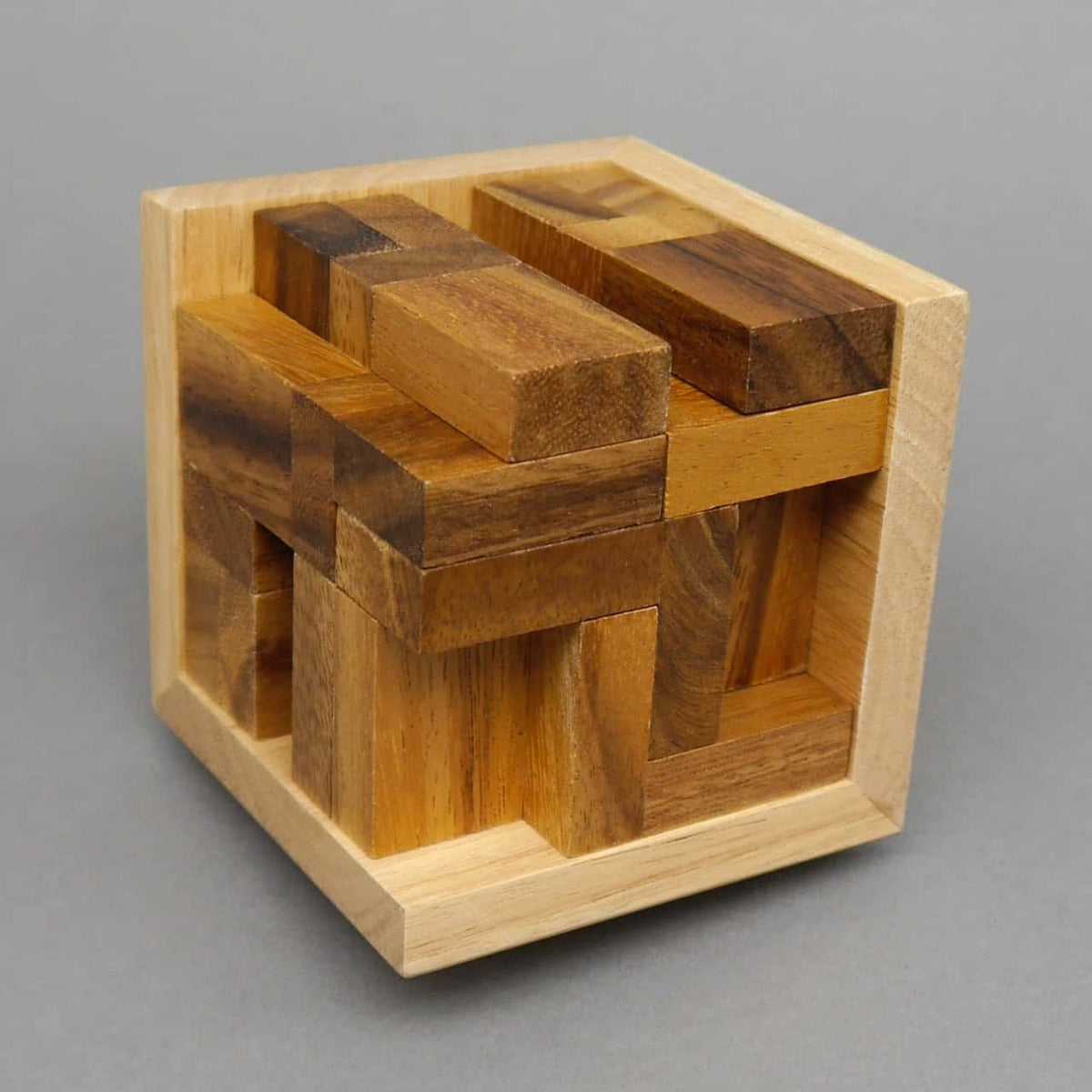 Holzbausteine bilden ein komplexes 3D-Puzzle in Würfelform auf neutral grauem Hintergrund.