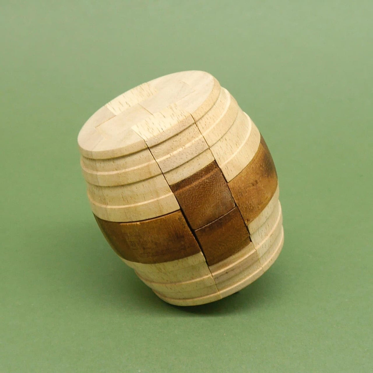 Fertig zusammengesetztes „Fass des Diogenes“ Geduldsspiel: zweifarbiges wooden Puzzle (Holzpuzzle) steht leicht schräg auf grünem Hintergrund.