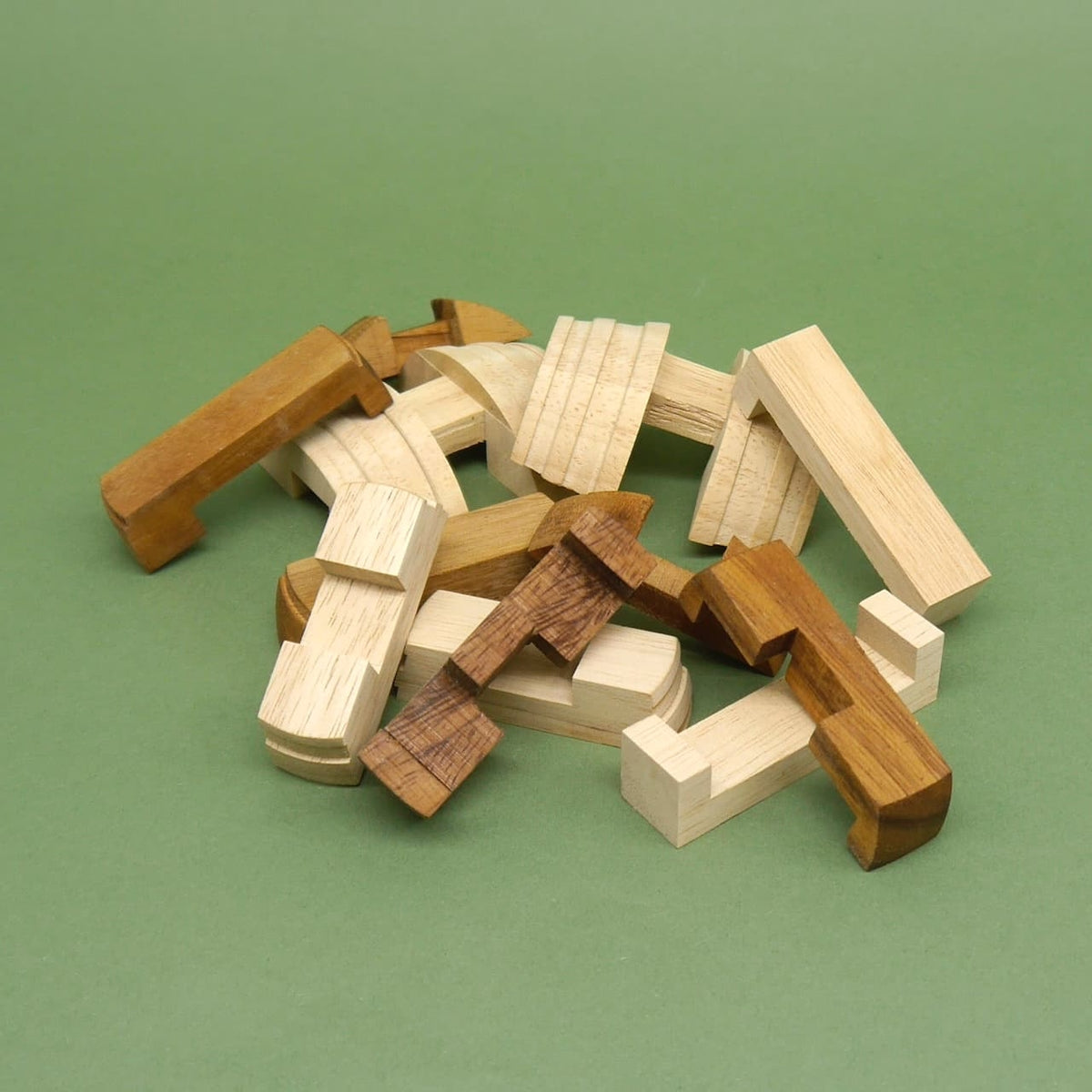 Lose verstreute Bausteine des „Fass des Diogenes“ Puzzle-Logikspiels: helle und dunkle Holzteile bilden das Denkspiel auf grüner Fläche.