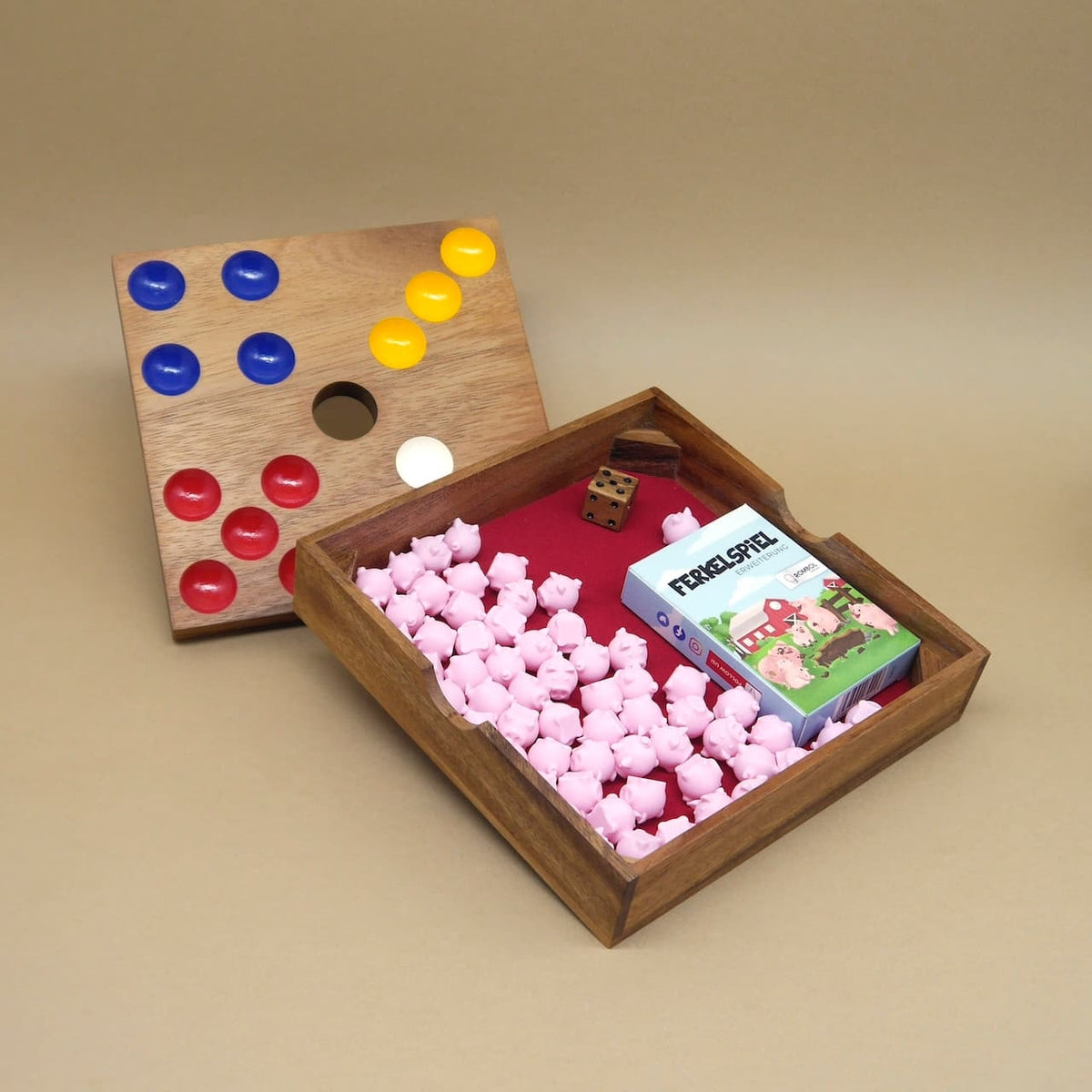 Offene Holzbox des Ferkelspiels mit Spielfeld, Würfel, Karten und rosa Schweinchen, beworben als Oink und Weg Brettspiel im Woodengame-Design.