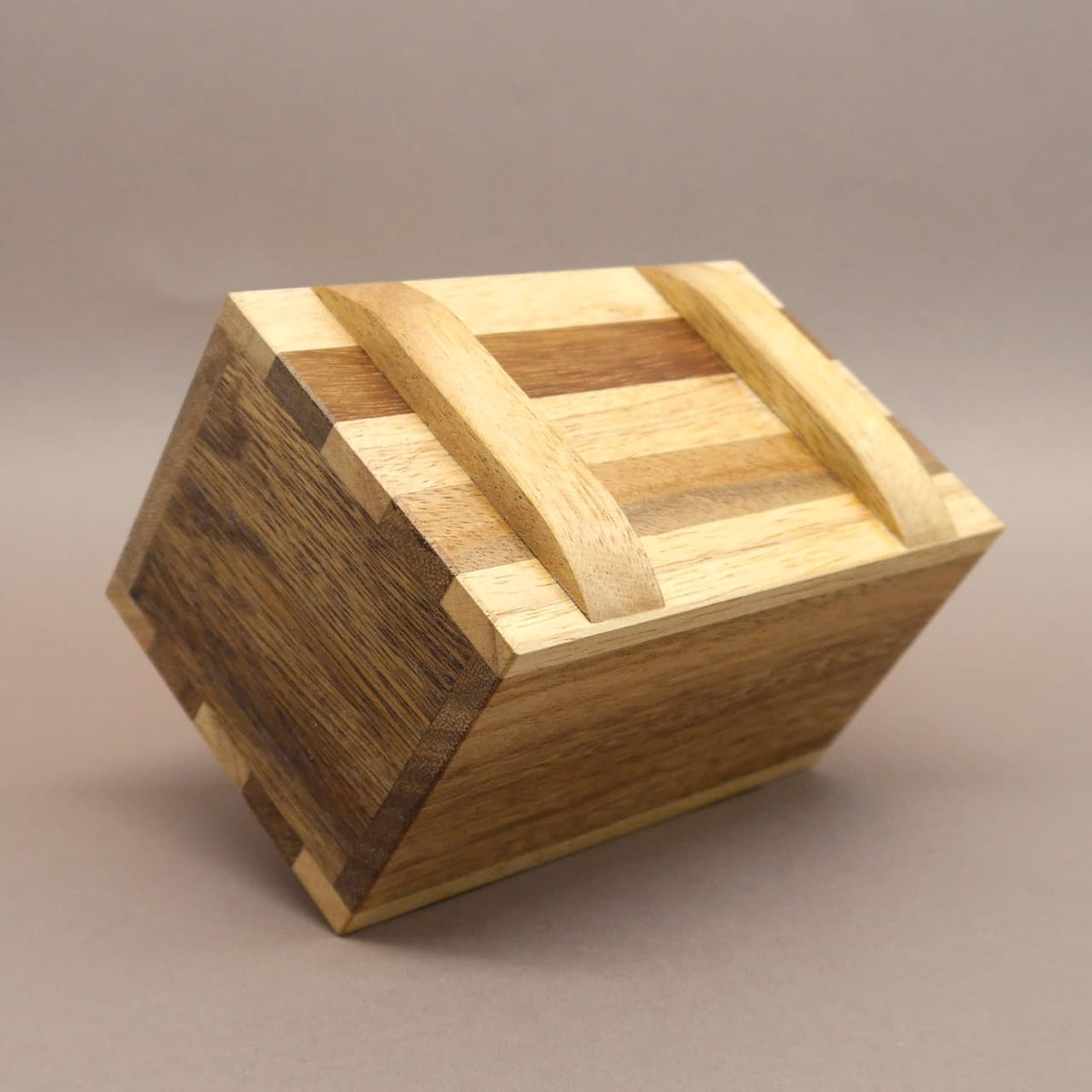 Geschlossene Geschenkverpackung aus gestreiftem Akazienholz; die rechteckige Puzzle‑Box liegt schräg auf der Kante.