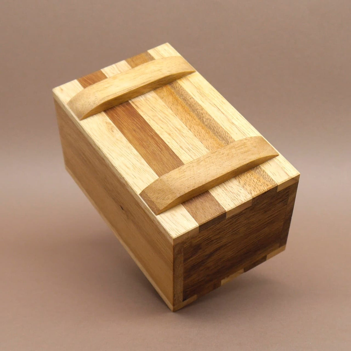 Zweifarbig gestreifte Holzbox aus Massivholz, leicht geneigt aufgestellt – eine dekorative Knobelbox.