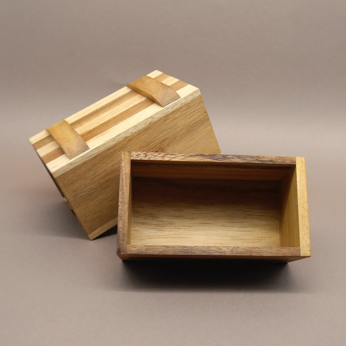 Geöffnete Woodenbox: Deckel und Unterteil aus hellem und dunklem Massivholz liegen getrennt und zeigen das Innere.