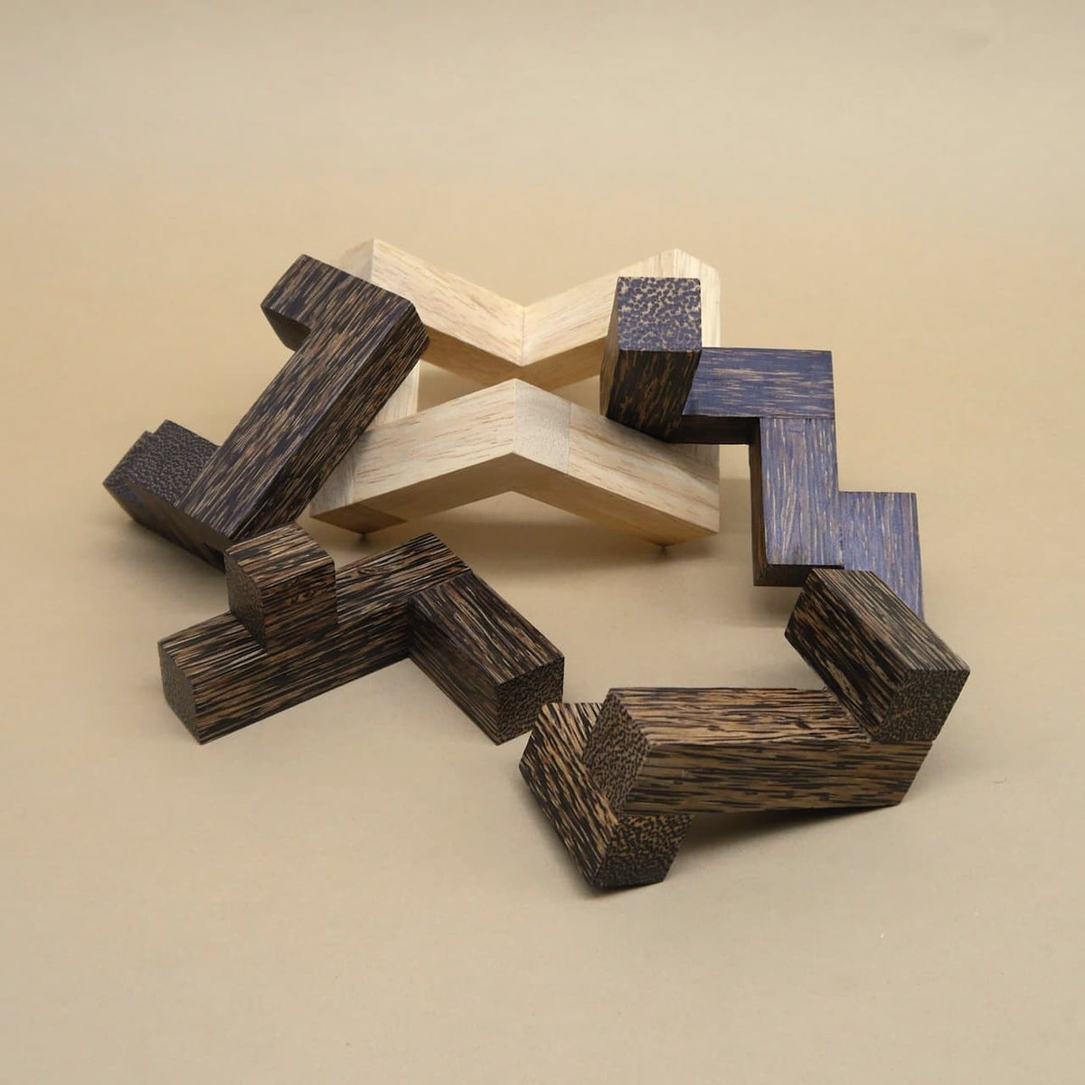 Ringförmig ausgelegte Teile eines Interlocking-Puzzle aus hellem und dunklem Holz liegen auf beigem Untergrund