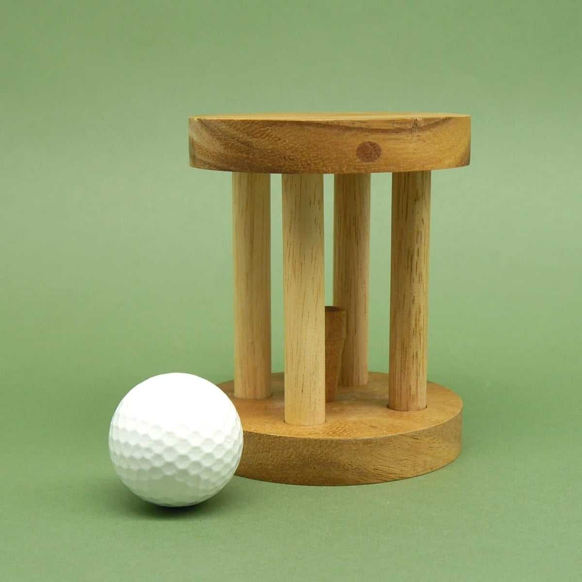 Denksport‑Puzzle aus hellem Holz mit vier senkrechten Stäben; ein weißer Golfball liegt gelöst davor auf grünem Hintergrund.