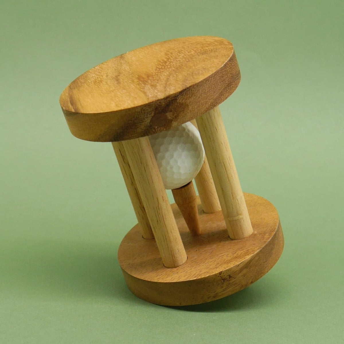 Schräg gekipptes Denkspiel‑Puzzle aus Holz, in dessen Mitte ein weißer Golfball auf einem Tee zwischen den Stäben steckt.