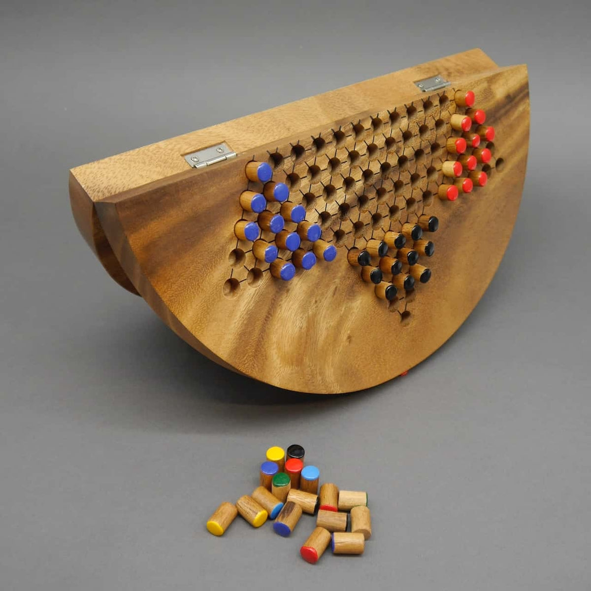 Ein zusammenklappbares Halma-Brettspiel aus Holz. Die Spielfiguren sind teilweise auf dem Brett platziert, während weitere Holzfiguren lose davor liegen. Das Brett zeigt Scharniere für die Klappfunktion, wodurch es leicht zu transportieren und aufzubewahre