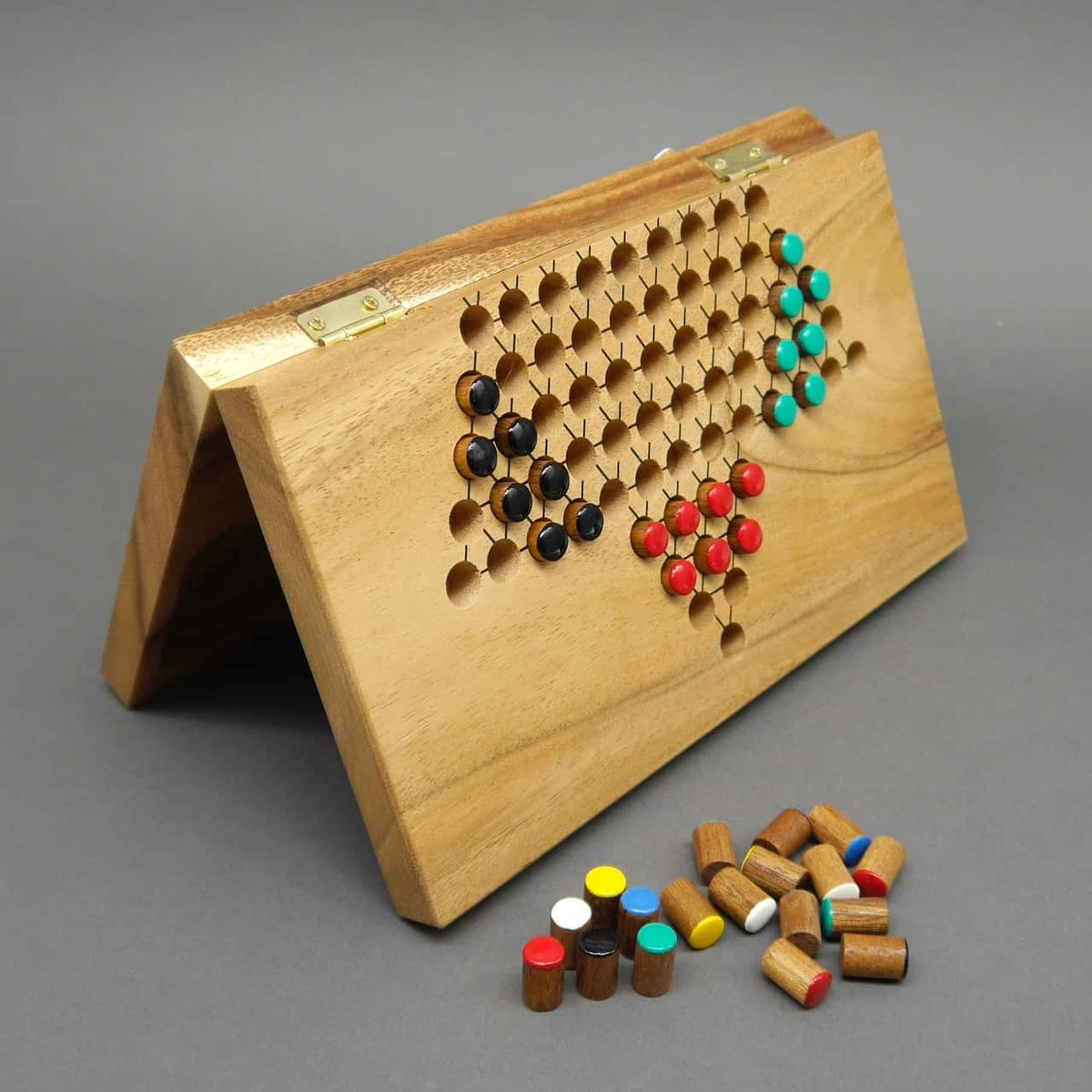Aufgeklappte Halma-Klapptafel aus hellem Holz, in deren runden Vertiefungen farbige Zylinderpöppel in Dreiecksformationen stecken.