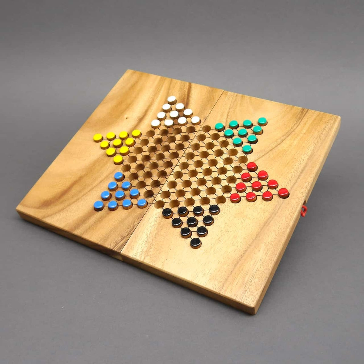 Flaches, quadratisches Halma-Brett aus Holz mit sechszackigem Stern, auf dem bunte Spielsteine für sechs Spieler startbereit liegen.