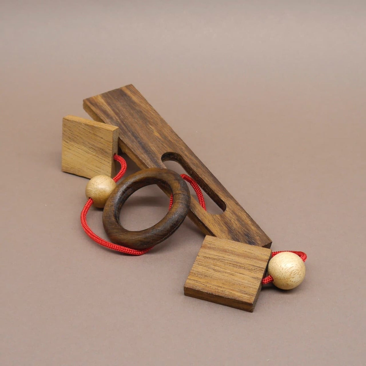 Handgefertigtes Kinderpuzzle aus Holz mit roter Schnur und geometrischen Elementen – fördert Logik und Geschicklichkeit.