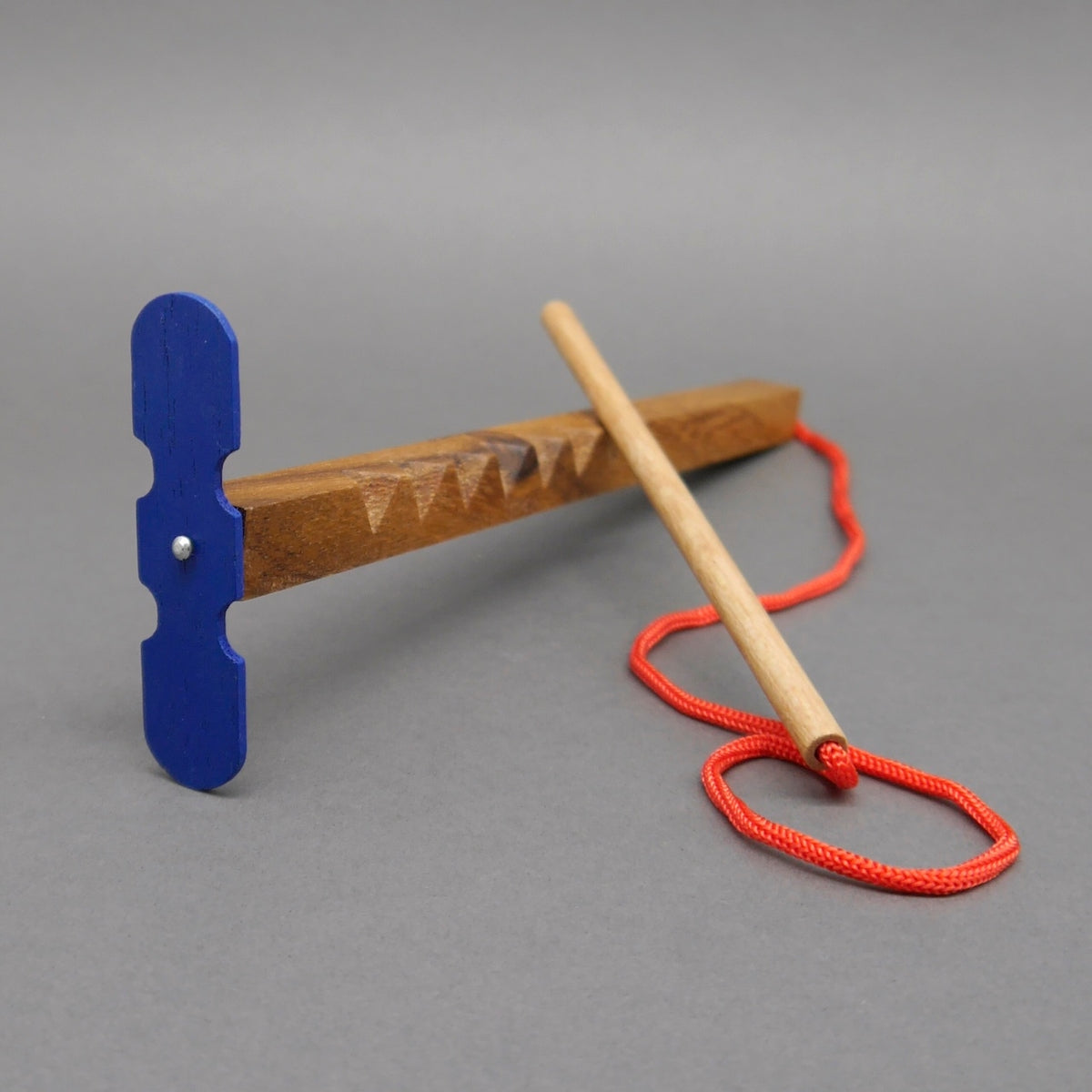 Hui‑Maschine Logikspiel Zaubern Knobeln: filigranes Holzspiel mit roter Schlaufe, Holzgriff und blauem Propeller‑Aufsatz.