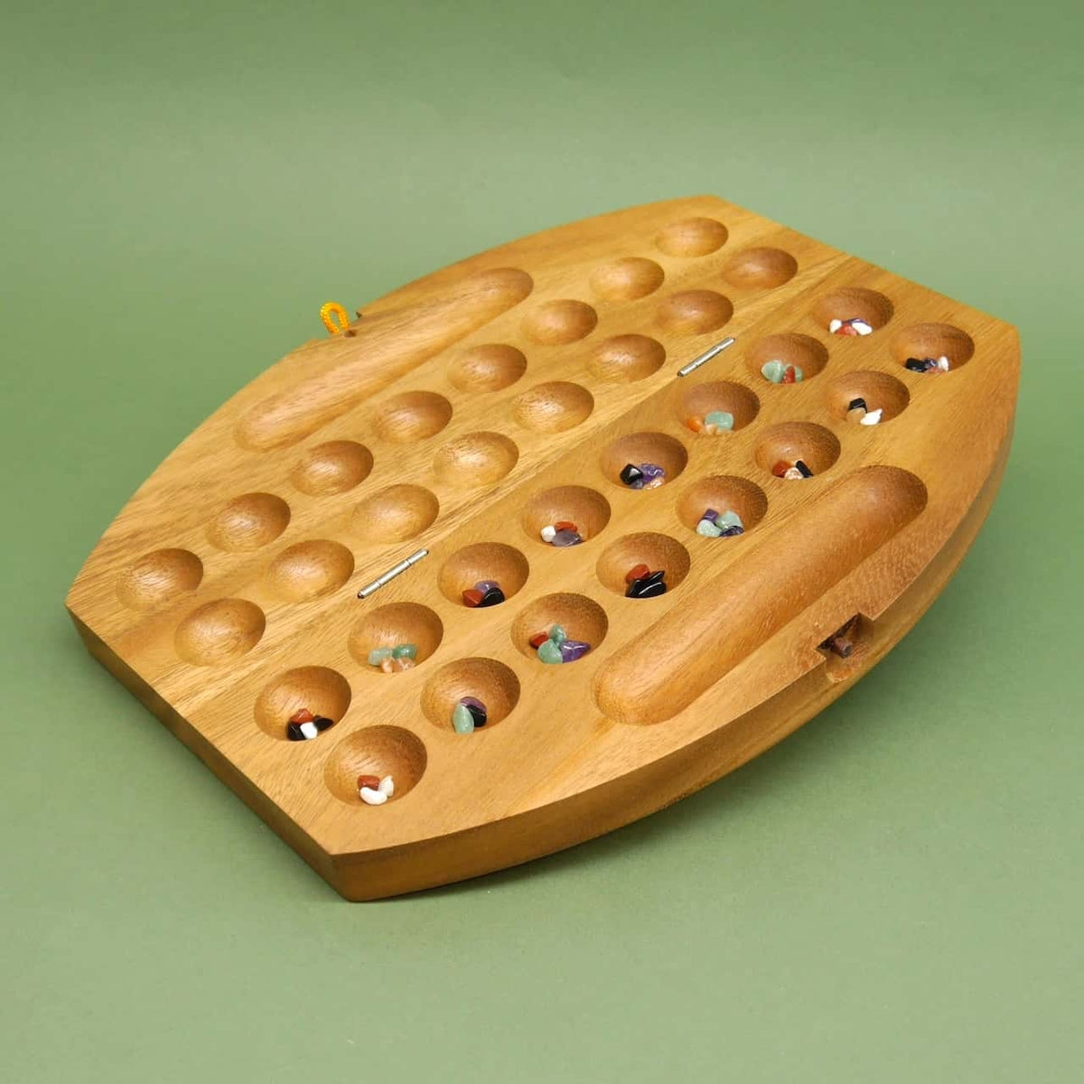Zusammengeklapptes Reisespiel aus hellem Holz, von einem roten Gummiband fixiert, auf grüner Fläche.