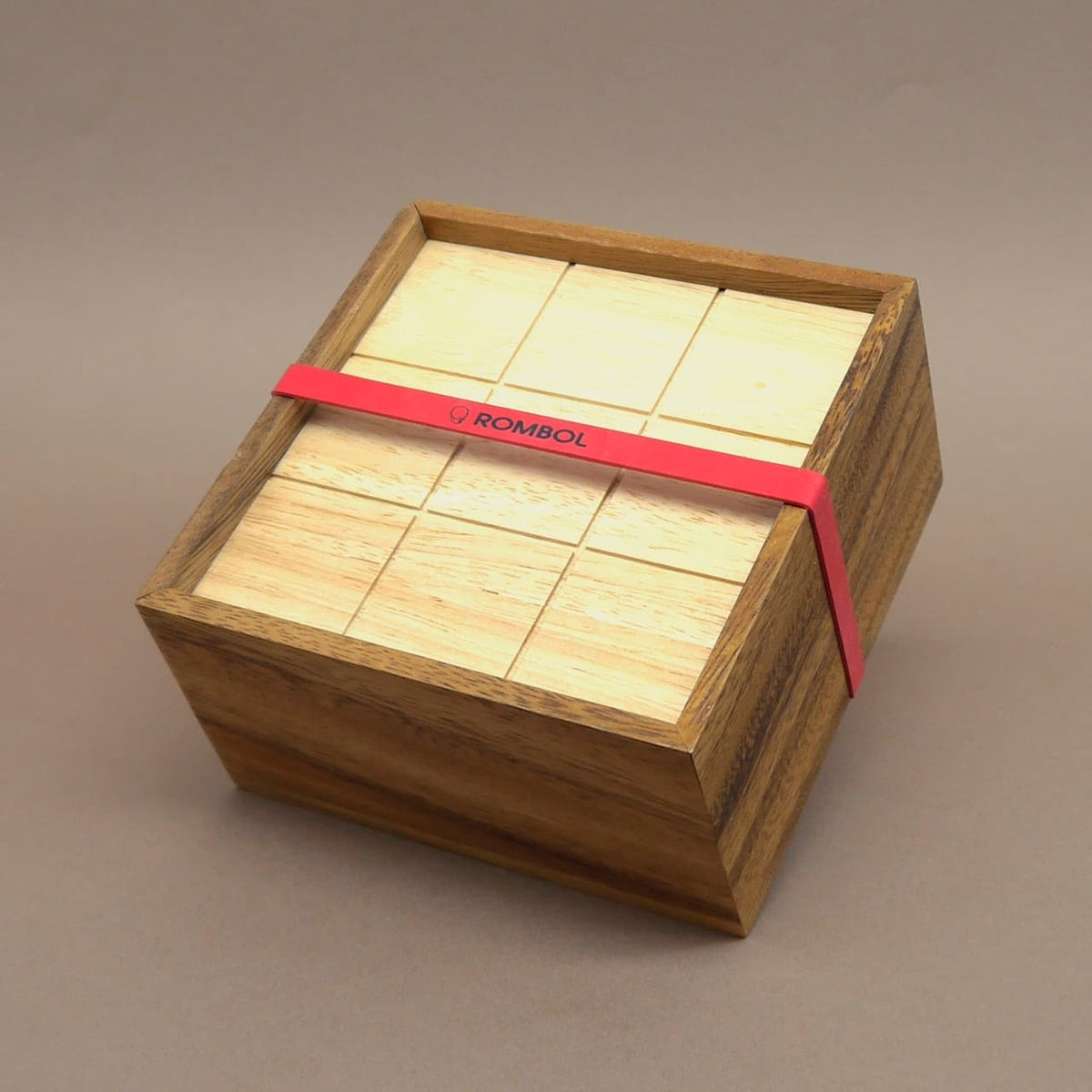 Holzspiel I Qube: quadratische Box mit Schiebedeckel und ROMBOL-Band – kompaktes Taktikspiel.