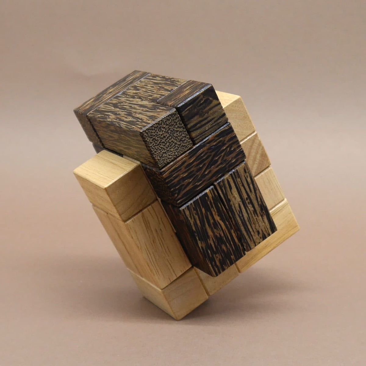 Holzpuzzle aus hellen und dunklen Quadern, zu einem komplexen Würfel zusammengesetzt und schräg auf einer Ecke balancierend.