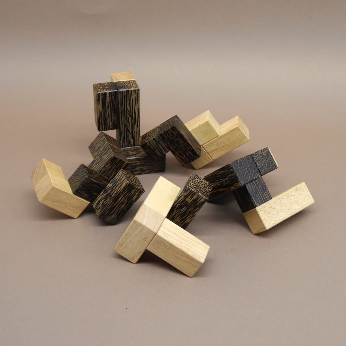 Locker verteilte Kettenstücke eines Logikspiels aus hellen und dunkelbraunen Holzklötzen liegen durcheinander auf neutralem Hintergrund.