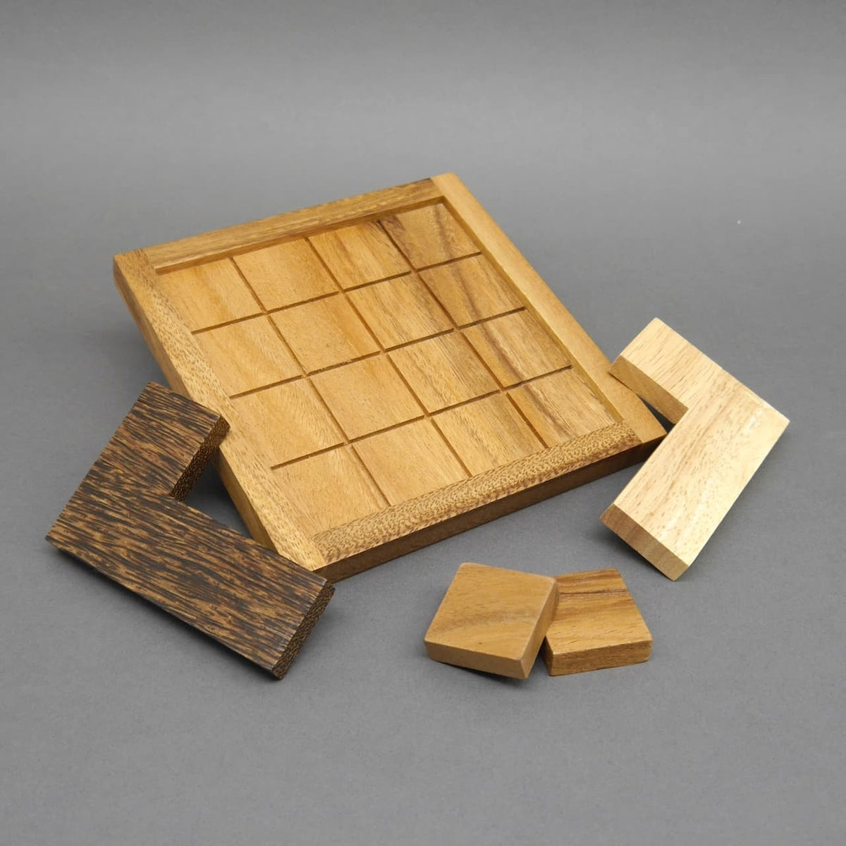 Beim brettspielen liegen zwei L‑förmige und zwei quadratische Holzsteine vor einem leeren, gerasterten Spielfeld.
