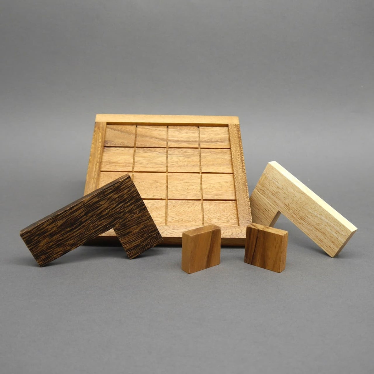 Vor einem leeren Holzbrett mit Raster wartet das strategiespiel mit zwei L‑Steinen und zwei kleinen Klötzchen auf den nächsten Zug.