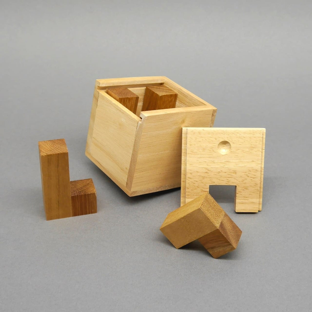 Teilgeöffnete Puzzlebox aus hellem Holz: geneigte Würfelbox mit Deckel und losen Bausteinen, einige Elemente noch im Inneren sichtbar.