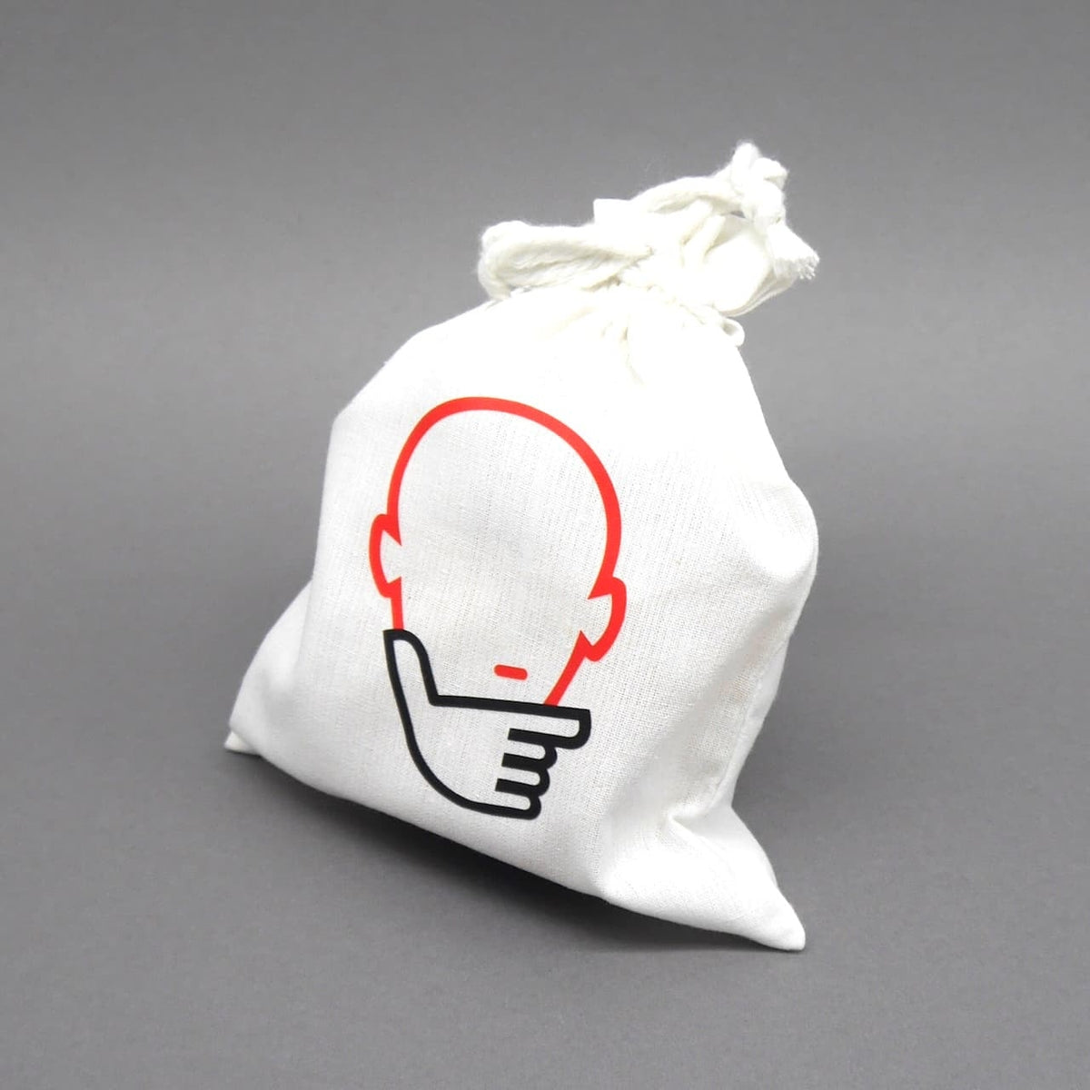Weißer Stoffbeutel mit Denkspiel-Logo: rote Kontur eines nachdenklichen Kopfes mit Handsymbol, stehend vor neutral grauem Hintergrund.