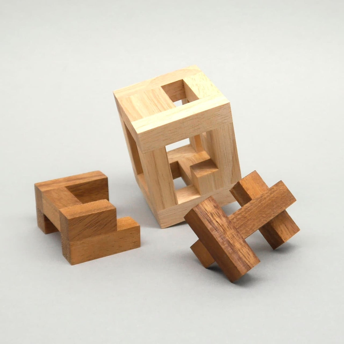 Offenes Woodenpuzzle als Logikpuzzle: Der helle Holzrahmen steht schräg, während zwei braune, verzahnte Elemente davor auf dem grauen Hintergrund liegen.