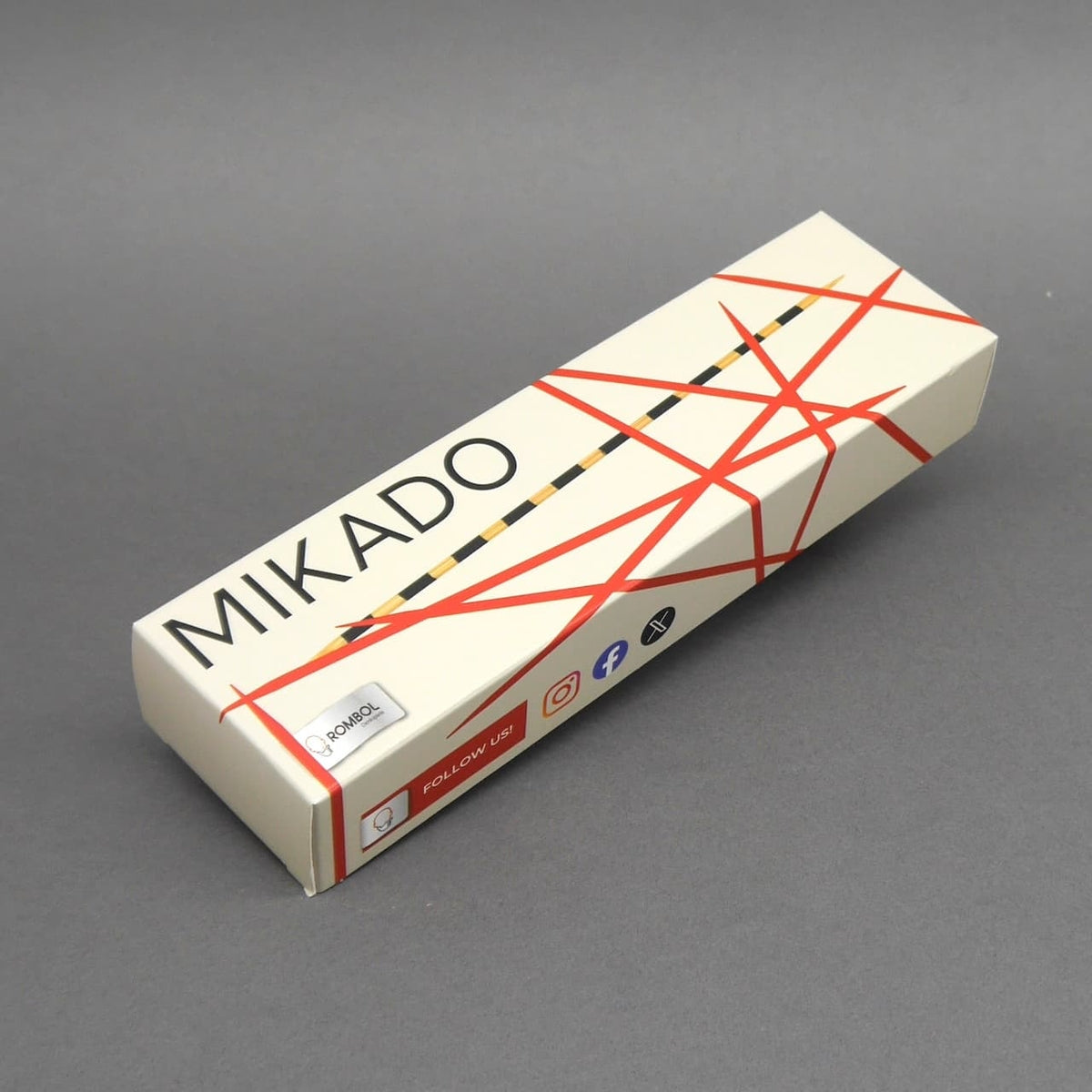 Hellbeige Mikado-Verpackung mit rotem Linienmuster und schwarzem Schriftzug, schräg auf neutral grauem Hintergrund fotografiert.