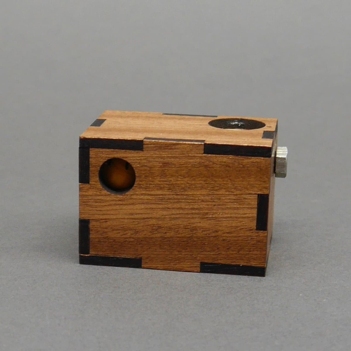 Packpuzzle „Minima Smiley“ als rechteckiger Holzkörper; seitliche Öffnung zeigt eine gelbe Kugel im Inneren.